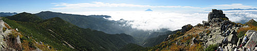 山梨県の金峰山から南を眺めた景色。画面中央の雲の上に、富士山が小さく見える。右端は五丈岩という風化した巨礫。