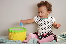 An infant engaging in play in Los Angeles, California (2015) Drummer girl (24186419196).jpg