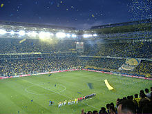 Un stade, en nocturne, présentation des équipes, alignées. Des papiers jaunes volent de partout. Dans le public, le jaune est majoritaire.