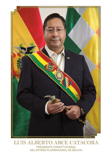 Full body portrait of Luis Arce, flanked by the Bolivian flag on the left and the Wiphala on the right.