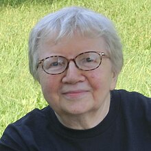 Porträt einer Frau mit grauen Haaren und Brille, leicht lächelnd