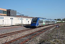 Train régional (engin thermique composé de trois caisses) s'approchant des quais de la gare, par temps ensoleillé.