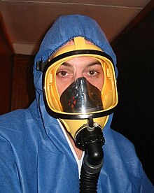 This full-face mask has an inner orinasal mask to reduce dead space, and, since it is being used against asbestos, exhalation valves (white). The hose connects to a PAPR filter-pump. Asbestos mask.jpg