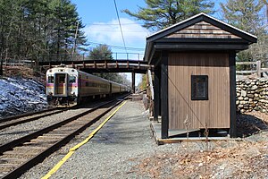 A passenger train passing a wooden shelter with a gravel platform