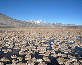 Photo of a mountainous landscape, with orange cylinders rising from a lake