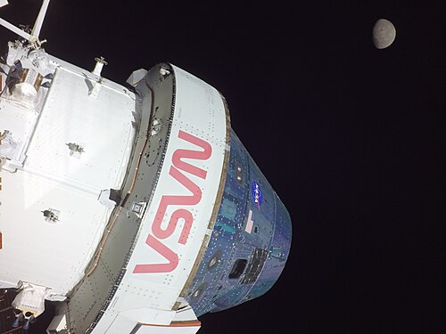Luna și capsula Orion în timp ce capsula se află pe orbită lunară; imaginea a fost realizată de o cameră plasată pe panourile solare ale modulului de serviciu european