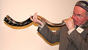 English: A man demonstrates sounding a shofar ...