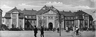 Quelques piétons et cyclistes déambulent devant la façade du Rigshospitalet (l'hôpital national) à Copenhague dans les années 1910.