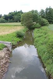 Koryto vodního toku, napravo louka, nalevo pole a betonové koryto, jímž přitéká potok od Bratronic.