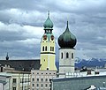 links: Stodpfarrkira St. Nikolaus, rechts: Heilig-Geist-Kira, im Hintergrund de Kampenwand