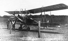 Biplane parked on landing ground, with three men standing beside it