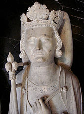 Kamenná busta sochy ležícího muže, která má na hlavě korunu a drží královské žezlo.