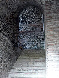 Vue d'un escalier s'engageant sous une voûte antique.