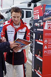 Earl Bamber wearing a red and white jacket and signing his autograph inside a book given to him by a spectator