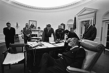 Un homme assis près d'un bureau discute avec des hommes debout