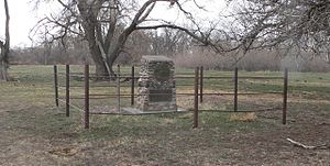 Stone monument about 3 feet high, on flat ground near wooded creek