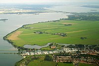 Op de voorgrond aan het IJmeer: Muiden met de Jachthaven Stichting Muiden, de thuishaven van de Koninklijke, en het Muiderslot. Links boven het midden het eilandje Hooft. Op de achtergrond: links de Flevopolder, rechts Muiderberg voor de Hollandse Brug, en het Gooimeer met het eilandje De Schelp (2007)