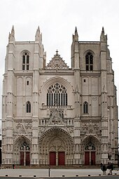 Façade : deux tours carrées encadrent la nef, bâtiment de style gothique en tuffeau blanc.