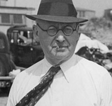 Photo d'un homme avec un chapeau et des lunettes qui fume une cigarette.