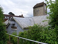 Very close view of a low iron church with a corrugated iron roof and a stone tower. This a low brown cap-style roof and a projecting crucifix..