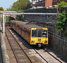 Желтый пассажирский поезд у каменной стены