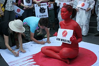 An oriental woman has painted herself red holding a sign (while sitting down) that says 