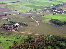 Ariel view of farming fields interspersed with roads, a small forest near the front of the photo