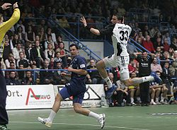 A handballplayer jumping towards the goal