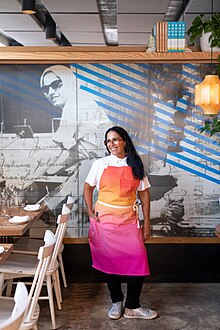 עינת אדמוני עומדת מול ציור קיר של אמה במסעדה שלה, "בלבוסטה", בניו יורק.