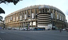 Vistas del Estadio Santiago Bernabéu en medio de una calle con coches y semáforos.