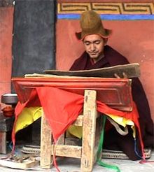 Буддийский монах Геше Кончог Вангду в красном одеянии читает сутры Махаяны на стенде