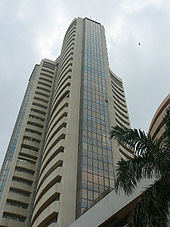 A skyscraper with curved walls and glass panes. A round building and a tree seen on its right side