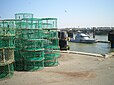 Des casiers de pêche sur un quai du port de Ouistreham avec, en arrière plan, le bateau de la Gendarmerie maritime.