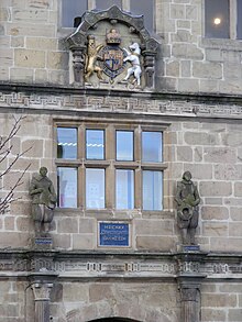 Две каменные статуи Филомата и Полимата в елизаветинских одеждах на первоначальных зданиях; также представлен в современной школьной библиотеке