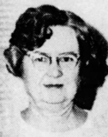 An older white woman with short wavy grey hair, wearing glasses