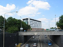 View of the ring road passing under a bridge, with a white office building and overhead signage visible in the distance