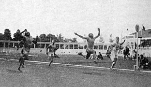 Foto de vários homens próximos de cruzar a linha de chegada de uma corrida, uma está no ar depois de um salto.