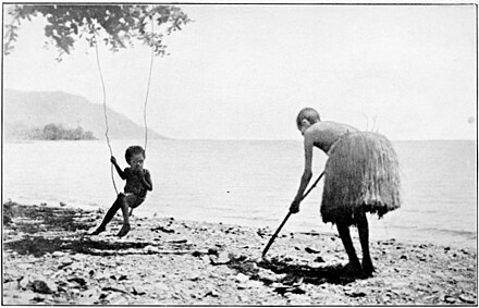 On a beach, a child on a swing and an adult poking the ground with a stick.