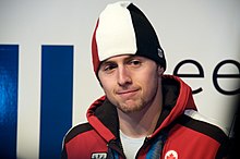 Photographie d'un homme avec un bonnet noir, blanc et rouge, veste rouge.