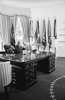 Gerald Ford sitting at a large mahogany desk in the Oval Office