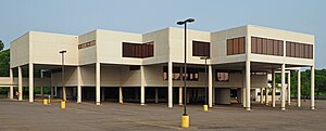 A white three-story building, where portions of the second and third stories are suspended over the parking lot on cylindrical supports