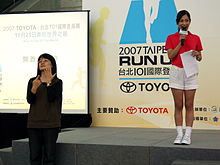 The hostess (in red) and a sign language interpreter at a press conference in Taipei, 2007 2007Taipei101RunUp PressConference SignLanguageInterpreter Host.jpg