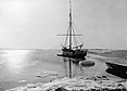 Das Schwarzweißfoto zeigt das Segelschiff Alabama vor der Insel Shannon ankernd. Am Ufer liegt Eis und rechts im Bild am Strand ein Ruderboot.