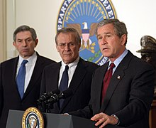 George W. Bush announces his $74.7 billion wartime supplemental budget request as Donald Rumsfeld and Paul Wolfowitz look on Bush War Budget 2003-crop.jpg