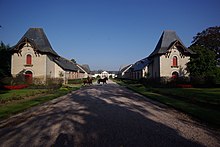 Large route entre deux bâtiments débouchant sur deux chevaux au fond