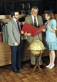 Two men and a young woman standing around a globe and looking at a red folder