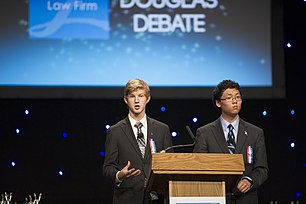 Two men wearing suits and ties stand at a podium facing the camera