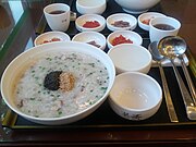 A bowl of Korean seafood juk with roasted ground seaweed and roasted sesame seeds and Banchan