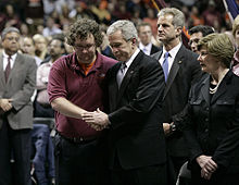 Президент Буш сжимает одну из рук студента обеими руками; Слева от него жена президента Буша, Лаура.