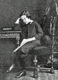 молодой парень в викторианском платье, сидящий за столом